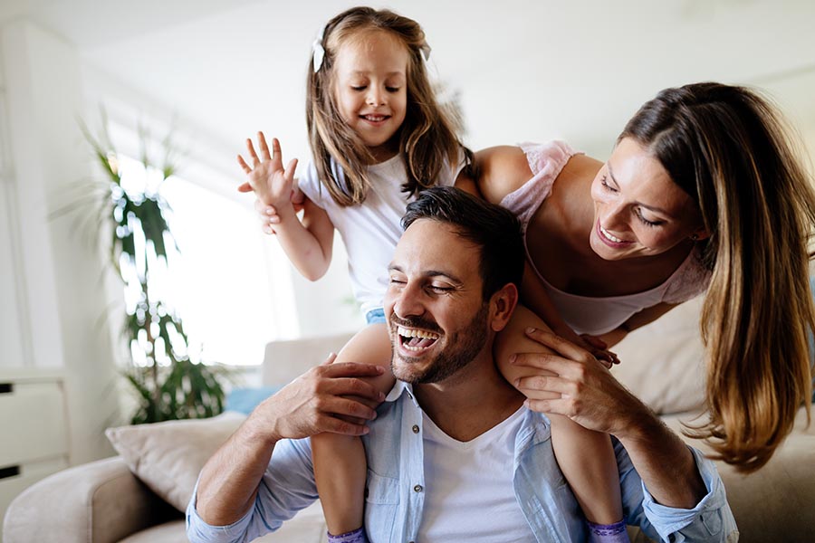 Personal Insurance - Young Family Laughing and Playing in Their Living Room, Daughter on Dad's Shoulders